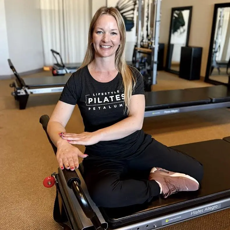 Woman sitting on Pilates reformer machine, smiling.