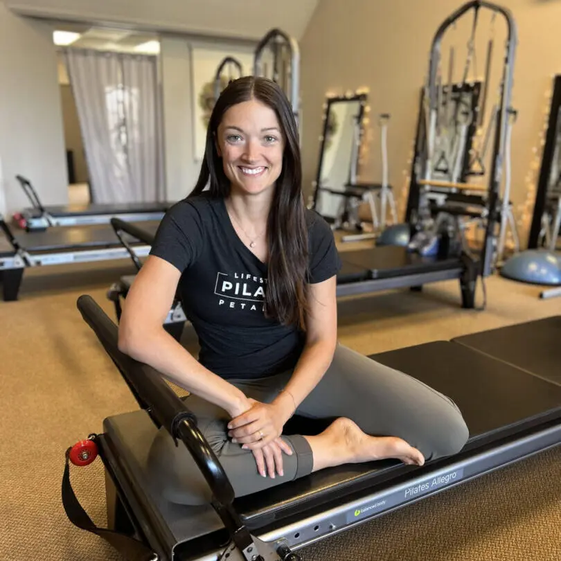 Woman smiling while sitting on Pilates equipment in a studio.